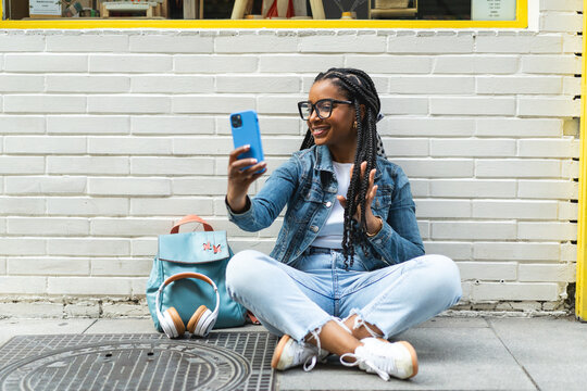 Smiling Latina woman with braided hair Sitting on the street using her smartphone