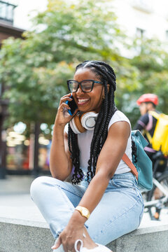 Smiling Latina woman with braided hair standing on the street using her smartphone