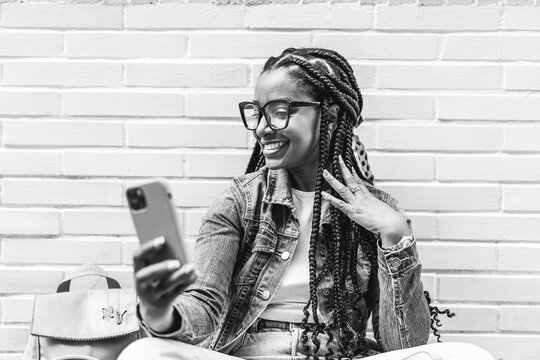 Smiling Latina woman with braided hair Sitting on the street using her smartphone