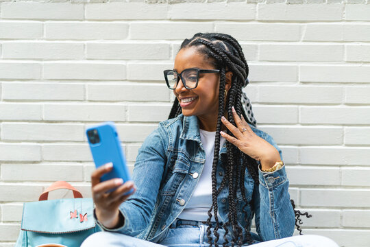 Smiling Latina woman with braided hair Sitting on the street using her smartphone