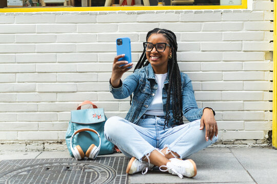Smiling Latina woman with braided hair Sitting on the street using her smartphone
