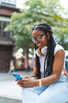 Smiling Latina woman with braided hair on the street using her smartphone