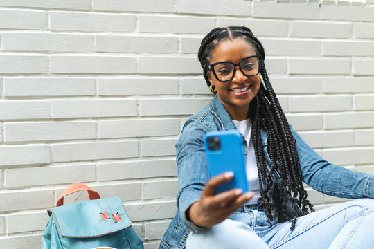Smiling Latina woman with braided hair Sitting on the street using her smartphone