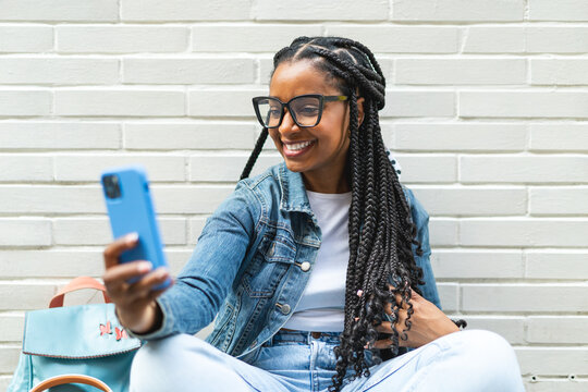 Smiling Latina woman with braided hair Sitting on the street using her smartphone