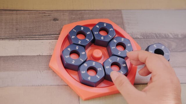 Hand placing numbered blue hexagonal puzzle pieces orange educational game board, developing logic and math skills, STEM toy, mental exercise, cognitive development, problem solving, matching numbers