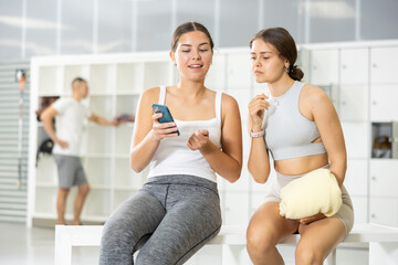 Young woman with mobile phone talking to friend in locker room after workout