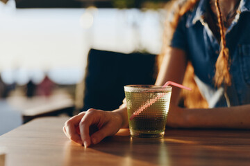 woman hand holding glass with green beverage on wooden table in warm sunny environment, casual moment of relaxation with natural light