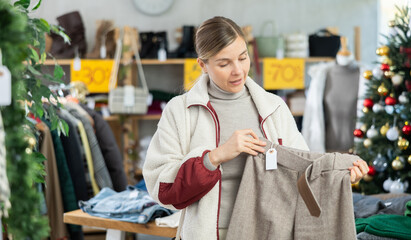 Uncertain young lady looking for trousers during X-mas sell-out season in retail outlet