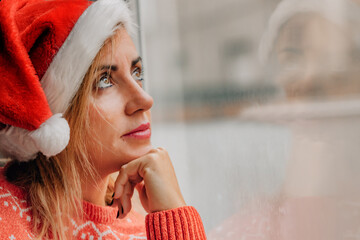 woman at home at christmas wearing a santa hat, looking out the window