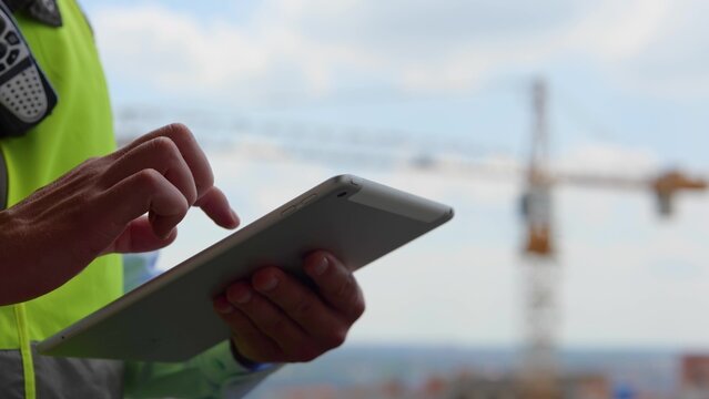 Close up of male hands holding tablet gadget tapping and scrolling on screen outdoors. Man builder engineer in uniform typing on device display with fingers, technology concept - Powered by Adobe
