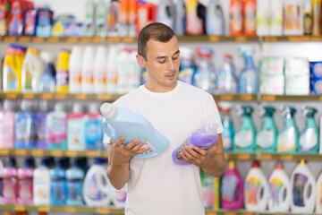 Man examines packaging of bottle with contents, reads information for consumer on label. Compares...