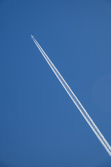 The plane flies, leaving a white trail in the blue sky