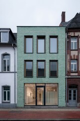 Obraz premium Modern green brick building contrasts with traditional architecture on a quiet street in a suburban area, showcasing a clean and unique design during overcast weather