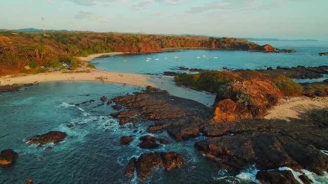 Aerial of sandy beach bay with anchored boats and rocky coast at golden hour