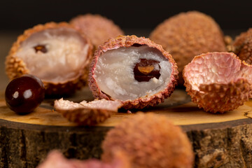 open red lychees cut into pieces on a wooden table, ripe lychee fruits with cut pink tough peel, cooking lychee