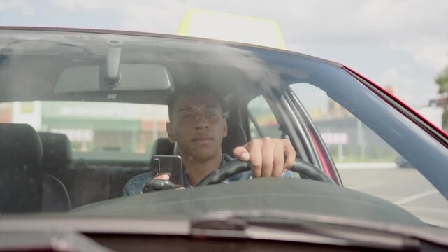 Male taxi driver looking at phone screen while driving car. Slow motion