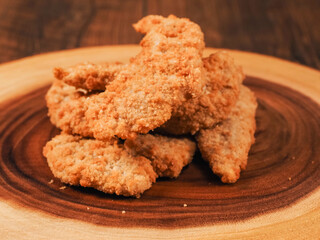 Uncooked chicken goujons or tenders on a wooden board. Popular classic chicken dish made from pieces of breast and breadcrumbs. Traditional ready to cook poultry product.