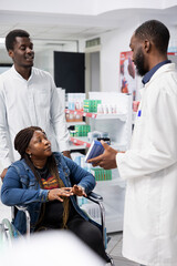 Obraz premium Pharmacist counseling a customer with disability on treatment options, discussing about medication dosage to support patient health. Professional medical staff showing drugstore pills.