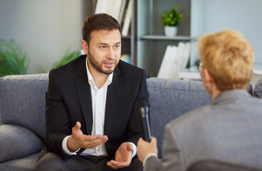 Businessman in interview speaks into microphone with journalist. He has focused conversation with...