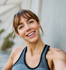 Fototapeta premium Young woman taking a selfie while posing against a wall after workout in athletic wear at urban location