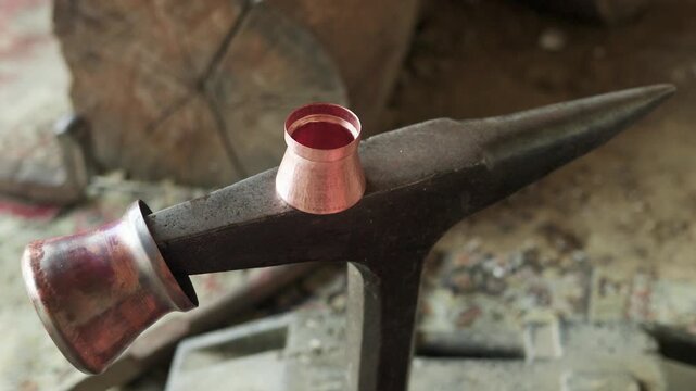 Romani coppersmith hitting a piece of copper with a hammer on a vintage anvil. Close-up view of the metalworking process in a workshop