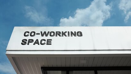 Co-working Space word sign displayed on the modern commercial building facade beneath a clear blue sky, signifying a facility dedicated to shared office space, collaborative work, and flexible rentals