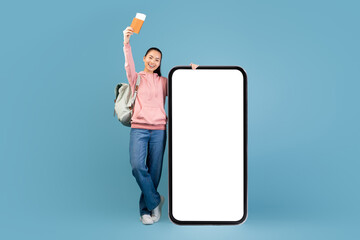 Young asian woman with a backpack expresses excitement for her upcoming trip. She holds flight...