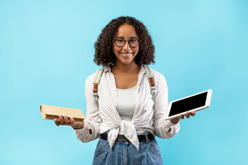 A black female student stands happily against a blue background, holding a digital tablet and a...
