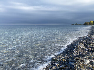 Tranquil rocky shoreline with clear water and overcast sky