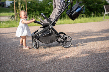 Obraz premium adorable child joyfully pushes a stroller outdoors on a sunny day, surrounded by greenery, capturing a moment of innocent play and exploration, carefree, moment, cherish, family, earth, warmth