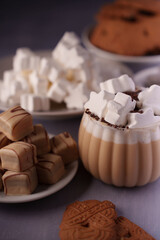 cozy table scene featuring a mug of frothy hot chocolate topped with marshmallows, alongside plates of bite-sized chocolate-coated caramel cubes and classic shortbread cookies, comforting, plated