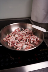 close-up of diced bacon pieces cooking in a stainless steel skillet on an electric stovetop, with a spatula nearby, in a modern kitchen setting, crispy, slices, greasy, process, texture, cutting