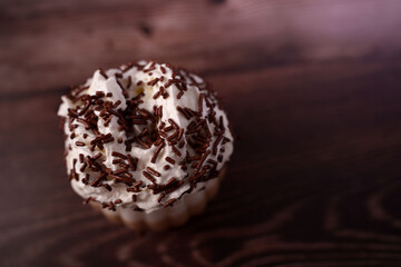 close-up of a chocolate sprinkle adorned cupcake on wooden surface with soft lighting creating a cozy, sweet, and inviting mood, inviting, cozy, browned, tasty, buttery, luscious, delight, texture