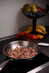 frying pan with cooking bacon on induction stove surrounded by fresh fruits and vegetables in a modern kitchen setting, household, electric, homely, casual, appetizing, ingredient, prepared, simple