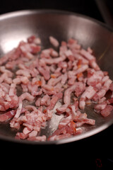 close-up of diced bacon sizzling in a silver frying pan under warm lighting, showcasing the texture and color of uncooked meat amidst the gleam of cooking oil, greasy, rich, pantry, glazed