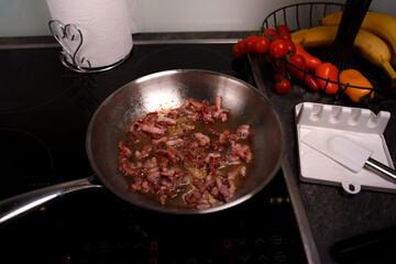 sizzling bacon cooking in frying pan with vibrant display of fresh cherry tomatoes, colorful bell peppers, and ripe bananas in modern kitchen setting with dark countertop, contrast, rustic, snack