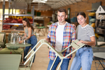 Interested couple, young girl and guy inspecting outdoor furniture at home and garden store,...
