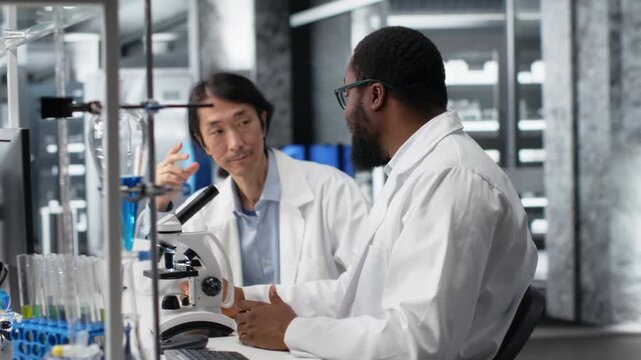 Diagnostic laboratory colleagues using microscope to evaluate cellular structures in lab. Clinical microbiologists observe medical tissue through magnification tool at laboratory bench