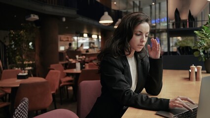 Young businesswoman working in the cafe at her computer looks very tired and feels pain in her head.