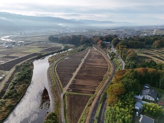 A river runs through a lush green valley with a town in the distance. The sky is overcast, giving the scene a peaceful and serene atmosphere