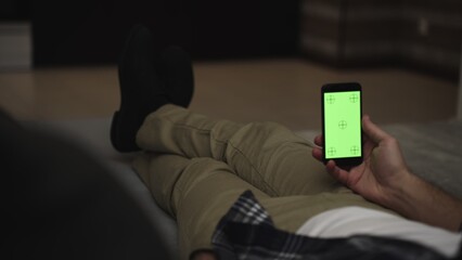 Man lying on couch using smartphone with chroma key green screen at night