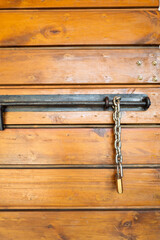 Vertical close-up of a rustic metal latch and chain padlock with visible screws, and aged metal, suggesting security and protection in a rural or traditional setting