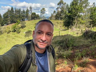 POV selfie of a happy smiling man with a backpack hiking outdoors in a sunny natural landscape. © Sergio Palacio