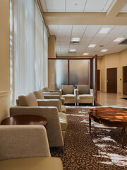 Modern medical center waiting room interior with neutral tones, upholstered seating, frosted glass divider, and natural light