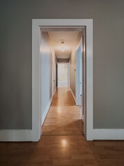 Straight view down narrow residential hallway with wood flooring, gray walls, white trim, ceiling lights and multiple doors inside an empty home