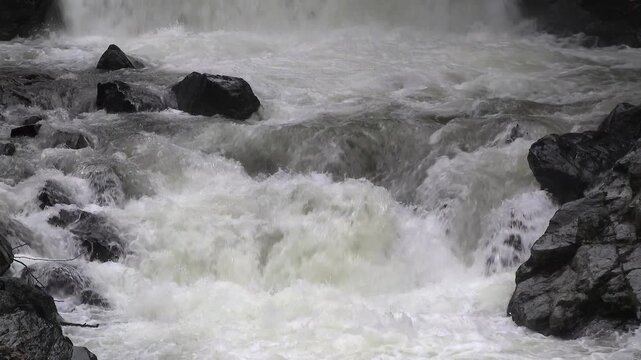 After waterfall foamy river flowing in narrow rocky valley. Slow motion capture of white water and bubbles rushing through a stony gorge.
