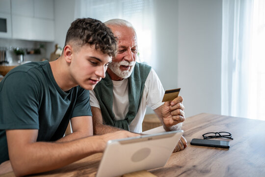 Grandson teaching grandfather online shopping using credit card