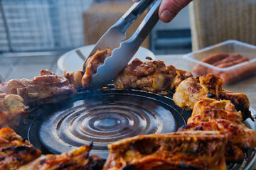 Grilled chicken barbecue cooking on outdoor charcoal grill with tongs, juicy roasted meat preparation on summer terrace, backyard bbq and homemade food concept