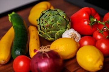 Fresh assortment of colorful vegetables including zucchini, artichoke, tomatoes, and peppers arranged on wooden surface, showcasing vibrant natural produce