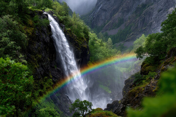 Fototapeta premium Majestic waterfall cascades with vibrant rainbow in lush green valley on a misty day